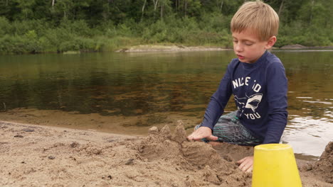 a little boy building a sandcastle on a beach on a summer camping trip in slow motion