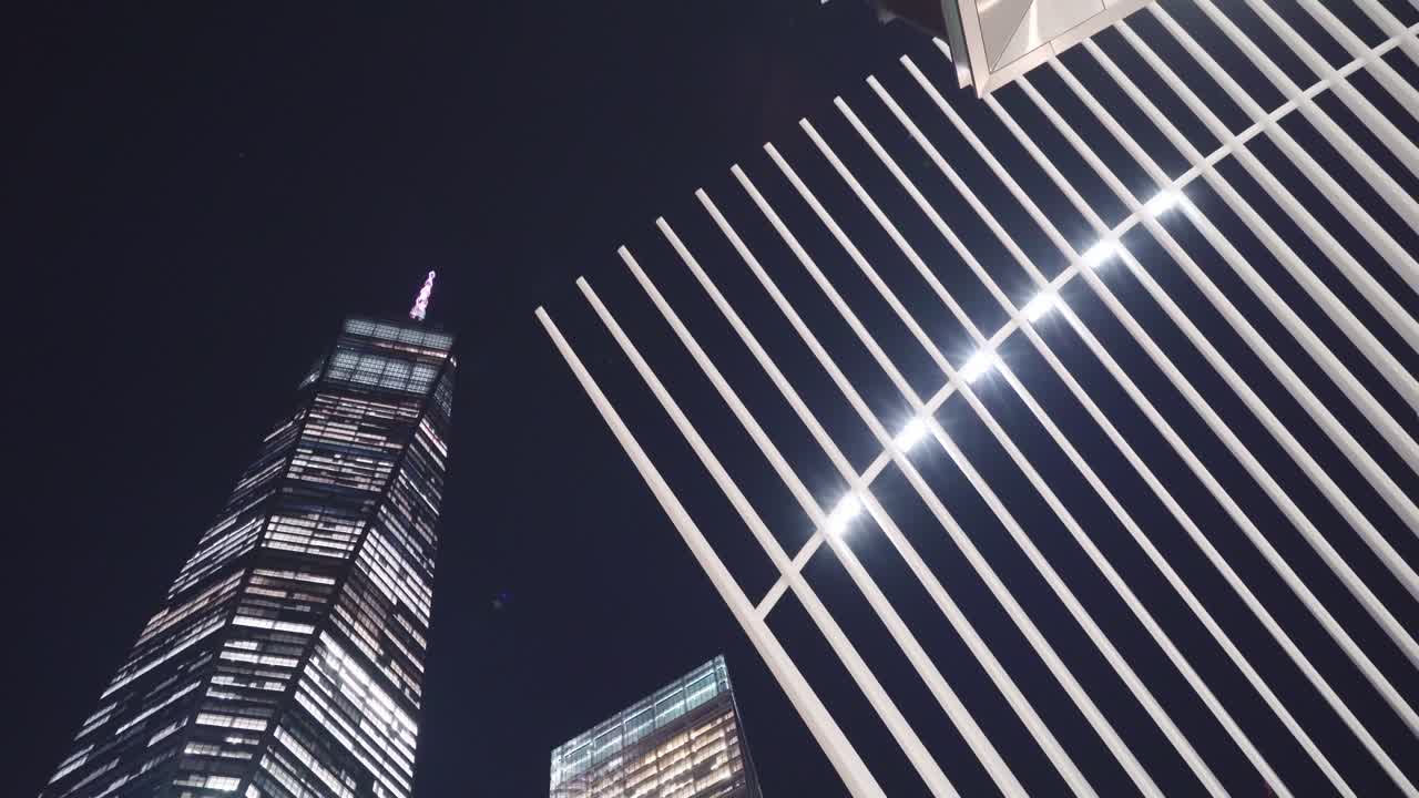 camera looking up to World Trade Centre Oculus and skyscraper One World Trade at night - streetlight passes by