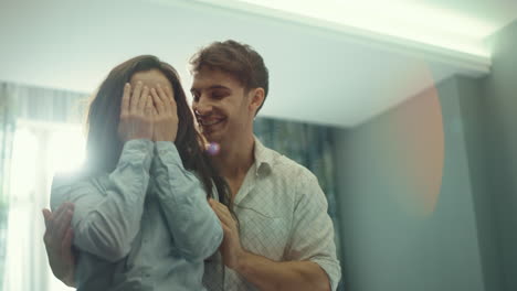 Lovely-man-making-surprise-for-girl-in-hotel-room.-Smiling-couple-having-fun.