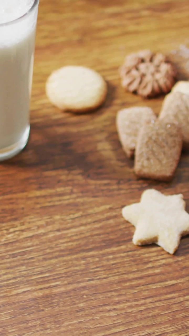 Biscotti e latte con bastoncini di cannella e formine per biscotti su un tavolo di legno.
