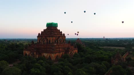 Aerial-of-ancient-temple-with-hot-air-balloons-flying-in-background,-sunrise