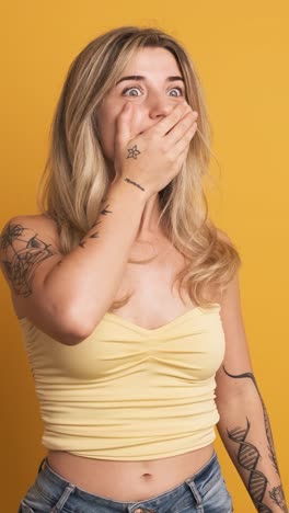 smiling young woman standing with widened eyes on yellow background