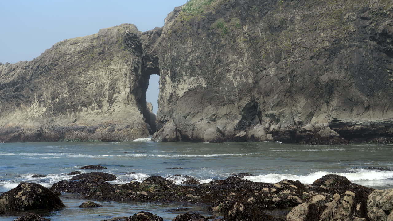 해초로 덮인 바위에 파도가 부서지는 열쇠 구멍 바다 아치 암석