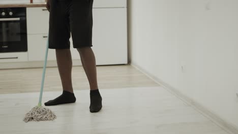 hombre negro limpiando el piso de la cocina con un trapeador. hombre serio lavando el piso en calcetines