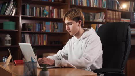 the guy is working on his laptop, sitting at a table in a chair