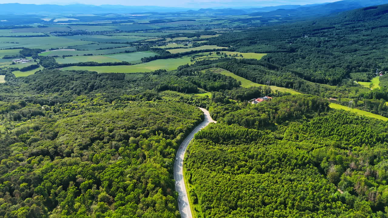 Winding road through lush trees. A lush green landscape showcases a winding road surrounded by forests and open fields under a clear blue sky