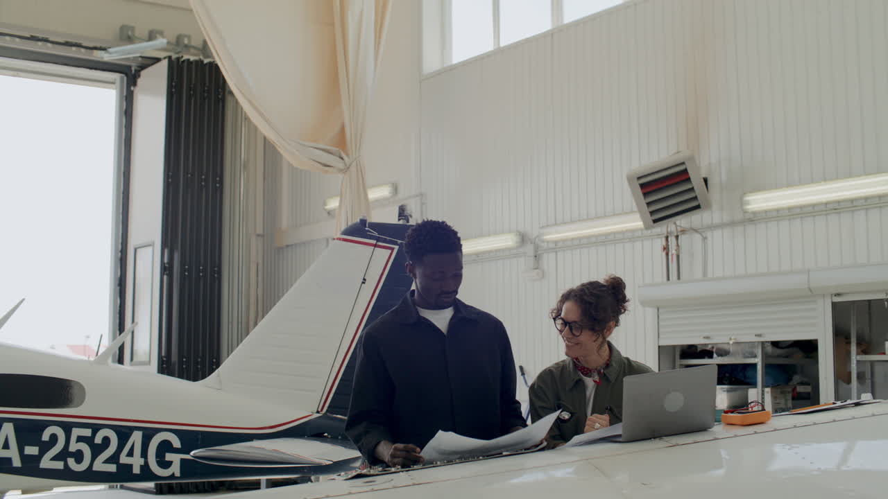 Two Diverse Engineers Analyzing Aircraft Schematics Together in Hangar