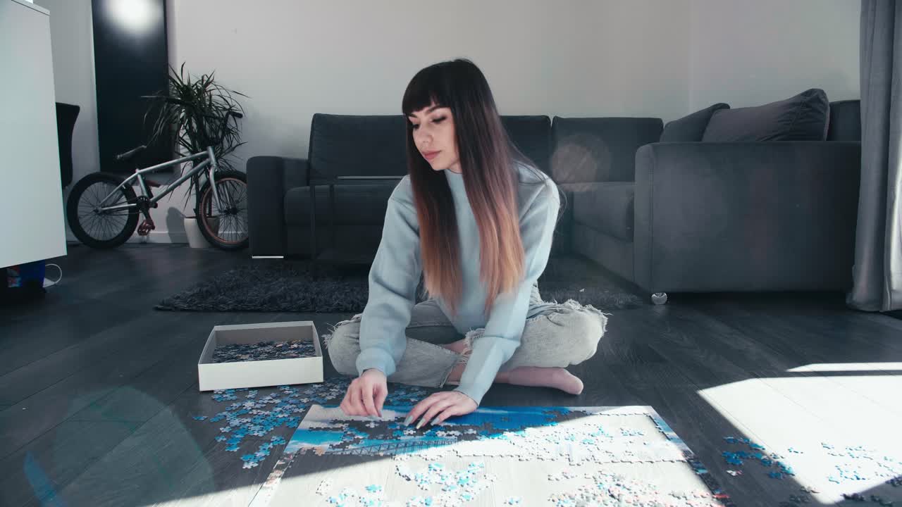 mujer joven sentada con las piernas cruzadas con ropa de moda de moda jugar solo piezas de rompecabezas conexión juntos en la sala de estar moderna con bicicleta estacionada en el fondo