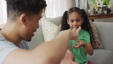 Happy-biracial-father-and-daughter-sitting-on-sofa-using-sign-language