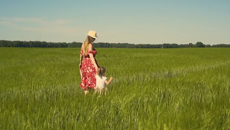 slow motion young mother in red dress which flutters in the wind dressing hat walks along the endless field