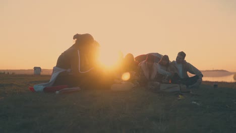 cheerful hikers rest at camping on river bank in evening