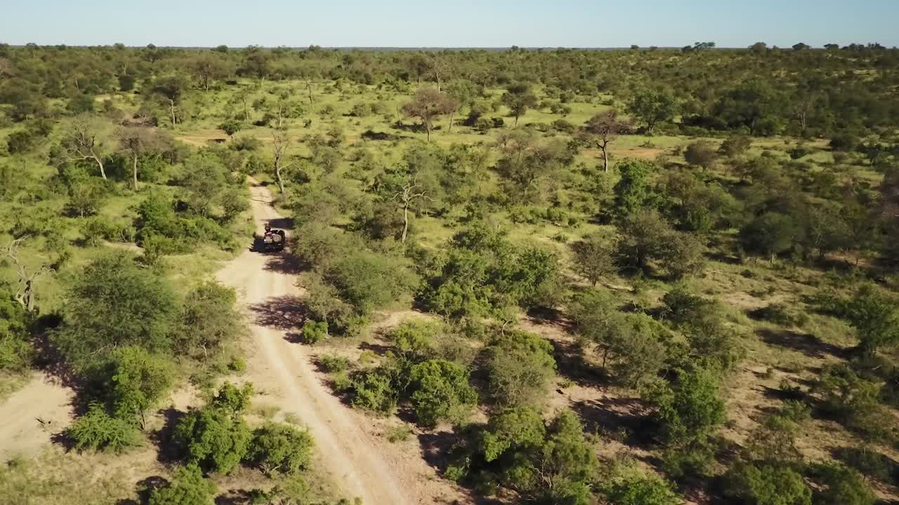 Ampia ripresa in movimento con drone di un veicolo da safari con ospiti che percorre una strada sterrata, mostrando l'ampio paesaggio africano.