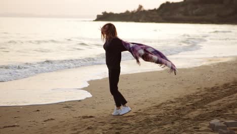 a woman whirling happily on the autumn seashore spreading hands covered with blanket