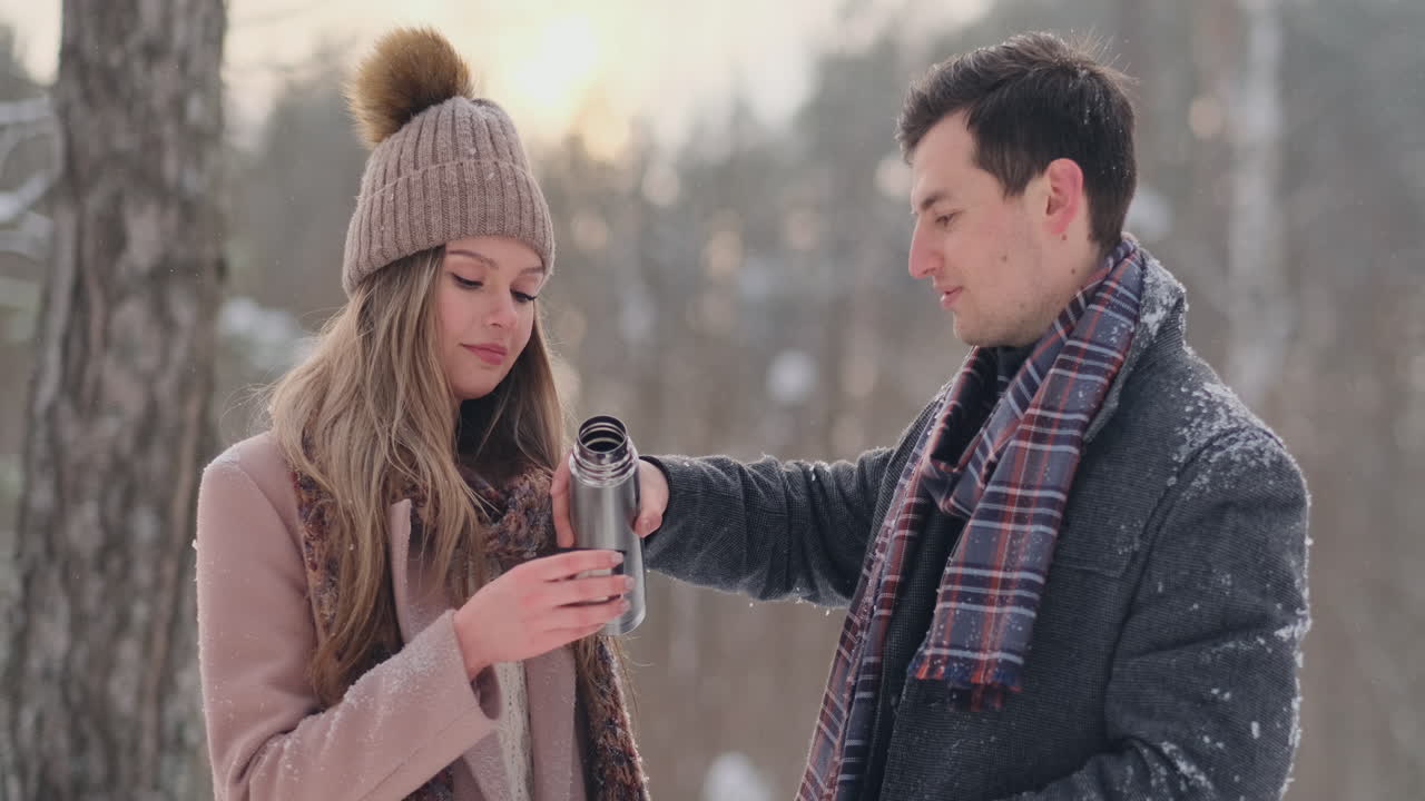 사랑스러운 커플 남자와 여자가 겨울 숲에서 보온병으로 차를 마시고 있습니다. 겨울에 공원에 코트를 입은 세련된 남자와 여자가 산책을 합니다. 느린