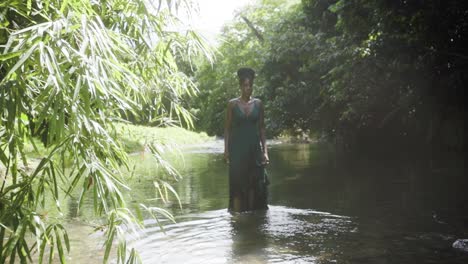 woman wearing a green dress stands deep in thought in a river