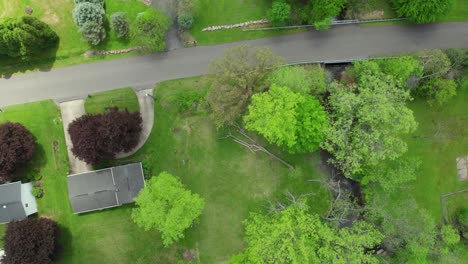 top down drone shot of creek stream running through residential neighborhood with bright greens in early spring