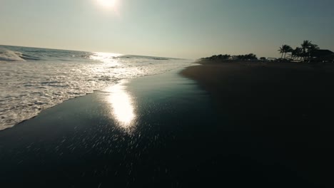 Volando-Sobre-La-Playa-De-Arena-Negra-Con-Olas-Salpicando-En-Monterrico,-Guatemala