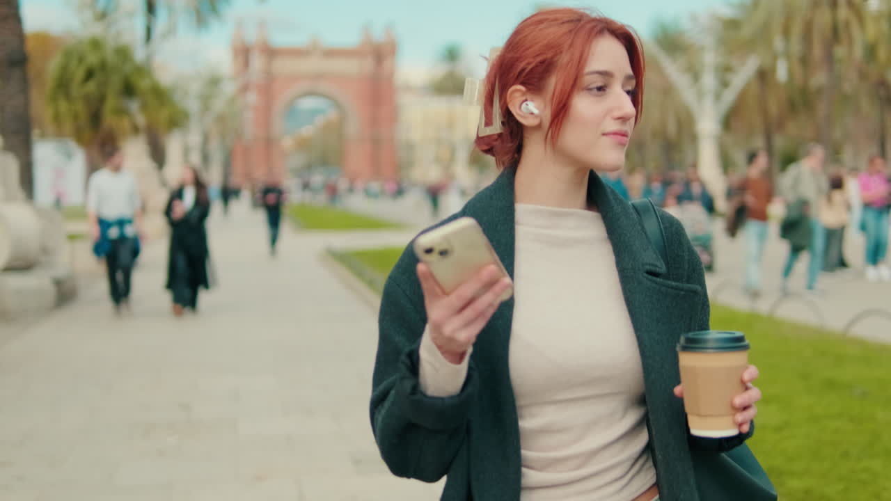 Young Red-Haired Woman Listening to Music with Earbuds in City Park