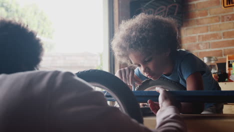 close up of pre-teen boy concentrating leaning down to concentrate on screwing in a bolt while building a racing kart with his father, selective focus