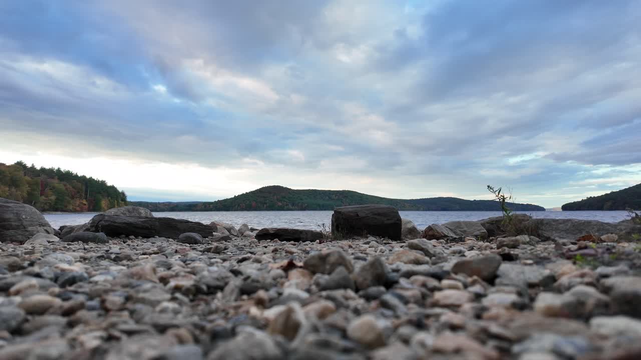 Paesaggio lacustre sereno con rocce e cielo nuvoloso.