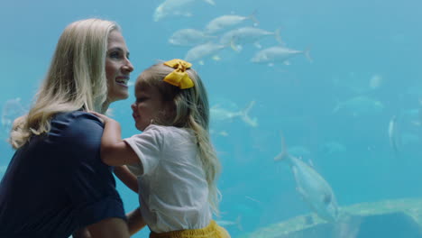 happy girl with mother at aquarium looking at beautiful fish swimming in tank child observing marine animals with curiosity having fun learning about marine life with mom in oceanarium