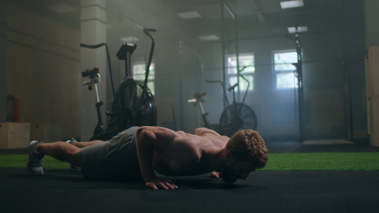 a strong man performs push-UPS from the floor with all his strength. a pumped-up man does push-UPS in the gym