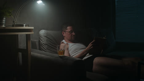 a sad man reads a book at night in his underwear