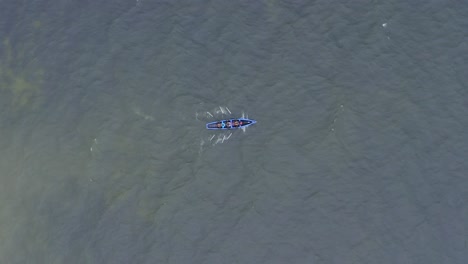 drone rotates above and follows currach boat rowers in open ocean water splashing