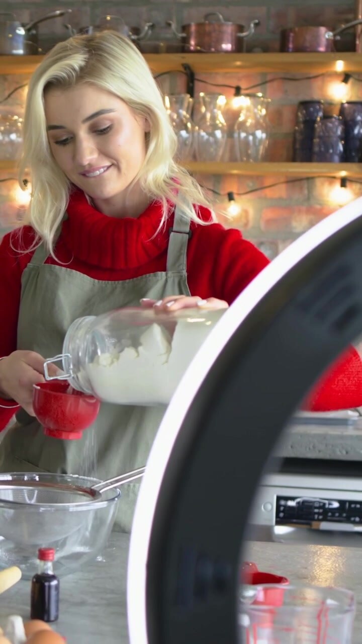 Video verticale: Donna in grembiule che setaccia la farina in cucina, con ring light accesa per la cottura