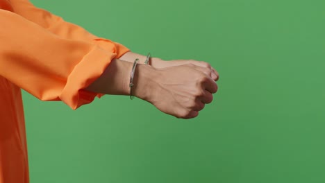 close up side view of male prisoner's hands in handcuffs being stretched out while he is standing on the green screen background