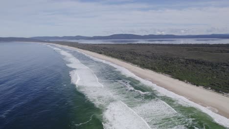 Schaumige-Wellen-Plätschern-Am-Sandstrand-Des-Seven-Mile-Beach-In-New-South-Wales,-Australien-–-Drohnenaufnahme-Aus-Der-Luft