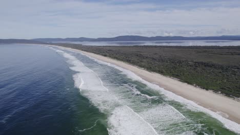 foamy waves splashing sandy shore of seven mile beach in new south wales, australia - aerial drone shot