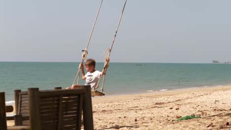 Niño-En-Un-Columpio,-En-La-Playa-De-Pak-Weep,-El-Mar-De-Andaman-En-El-Fondo,-Día-Soleado,-En-Khao-Lak,-Tailandia---Cámara-Lenta