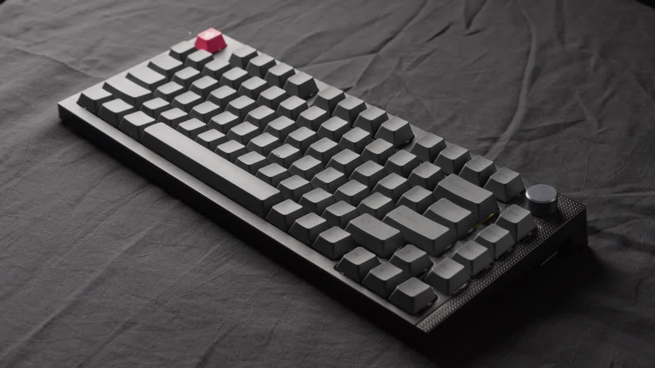 teclado mecánico gris colocado sobre un fondo de tela negra con un haz de luz móvil