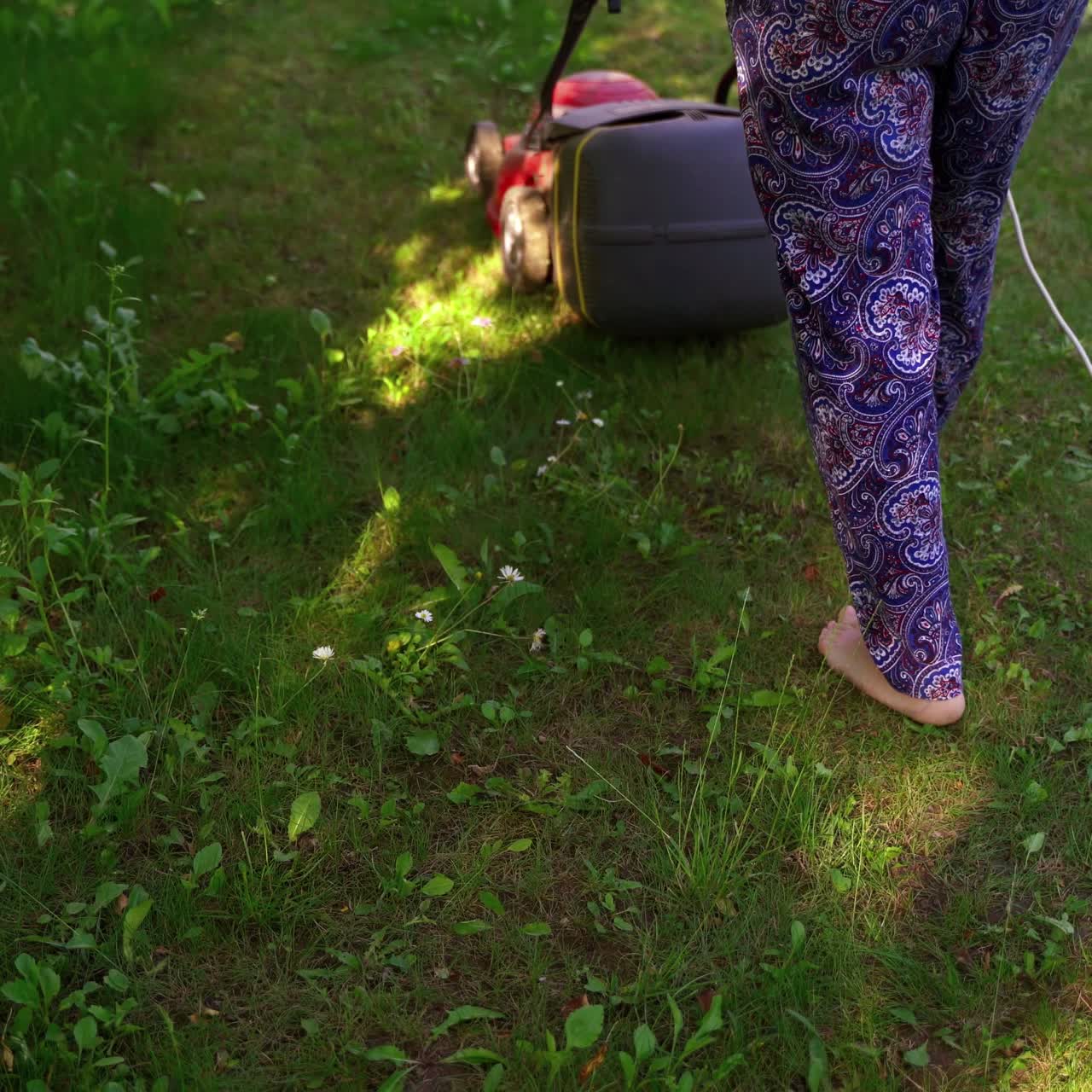 Woman work with lawn mower. Trimmer machine cutting green grass in the garden. Garden work in summertime.