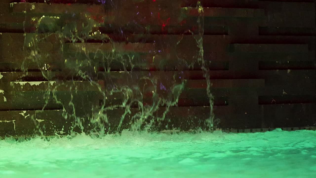 Water cascades into a glowing pool, night setting, steady camera, ambient artificial lighting