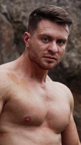caucasian sportsman with bare chest stands in the rock. athlete flexing muscles to show his athletic build. close up portrait. vertical video