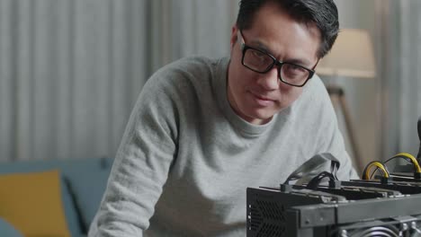 primer plano de un hombre asiático con gafas sonriendo a la cámara mientras usa una computadora portátil y una plataforma de minería para minar criptomonedas