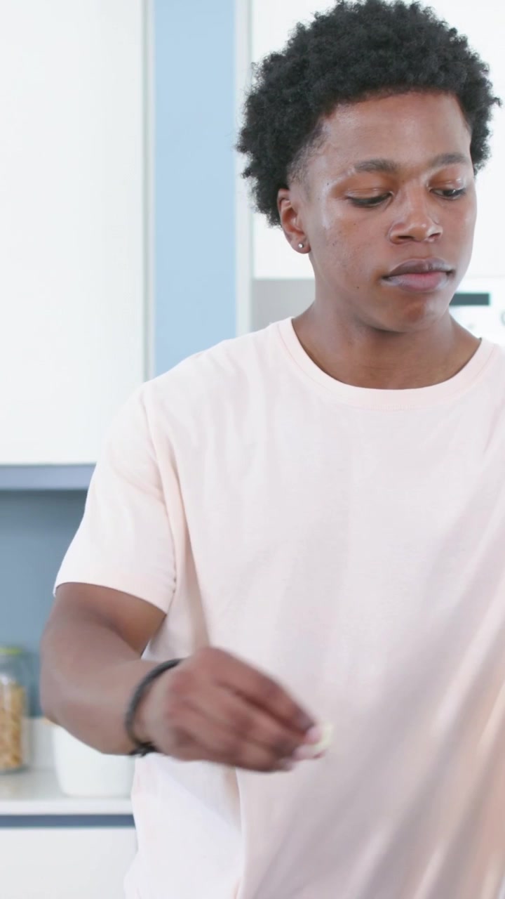 Vertical video: Reaching man in pink tee opening canister in kitchen, scooping contents for meal