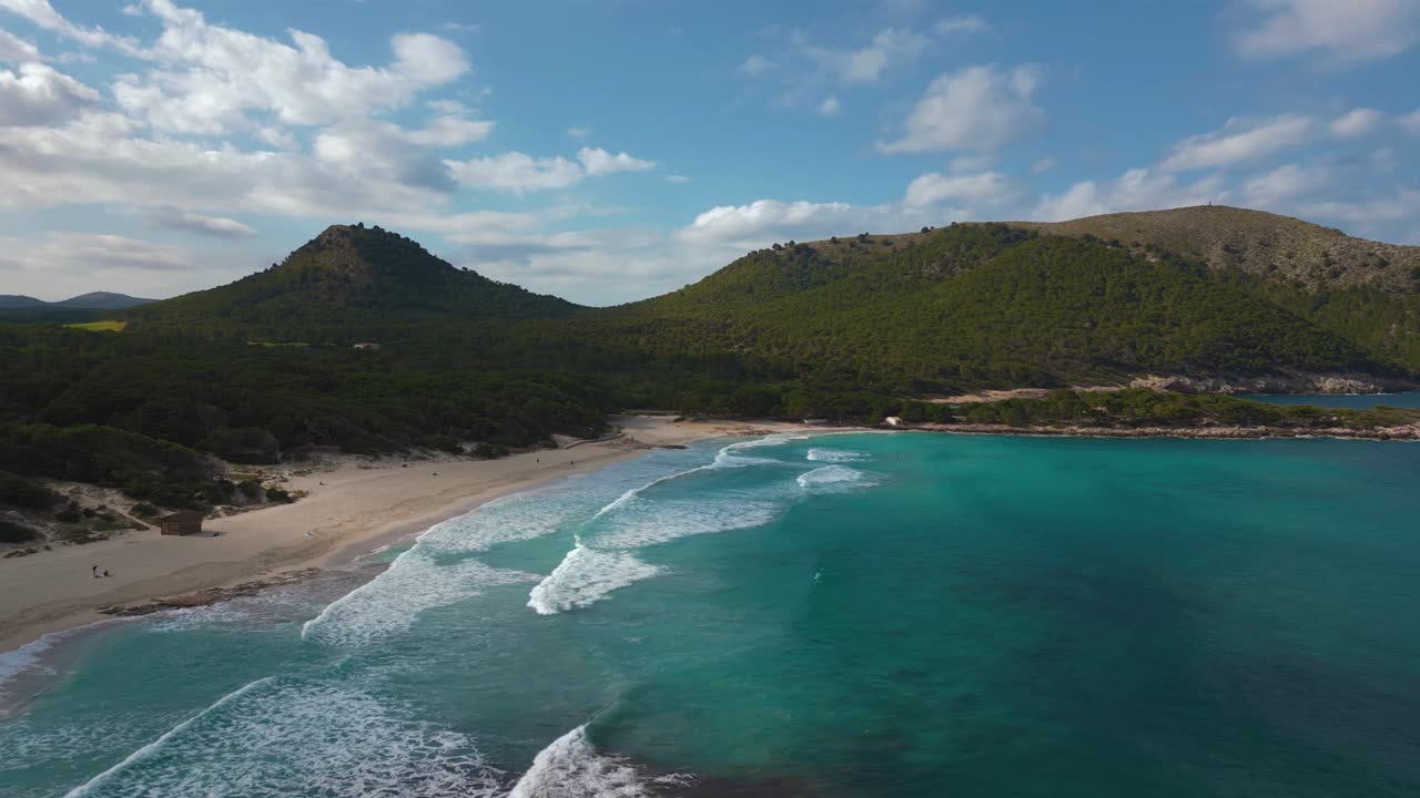 Baia tropicale con spiaggia sabbiosa, acqua di mare blu turchese cristallina, sabbia bianca e colline verdi.