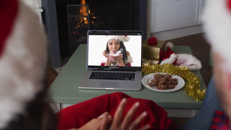 vista trasera de una pareja caucásica con sombreros de santa haciendo una videollamada en una computadora portátil durante la navidad