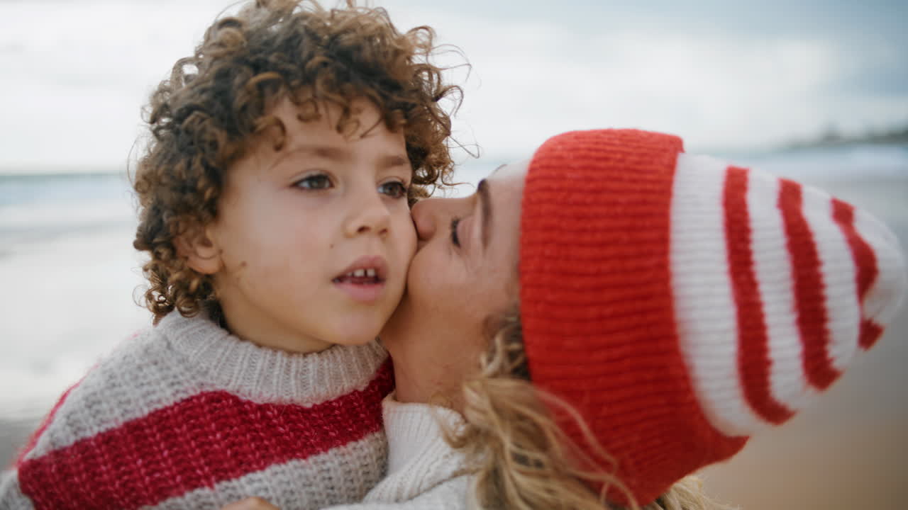 closeup madre acurrucando niño en traje de punto. familia linda descansando fin de semana en la playa