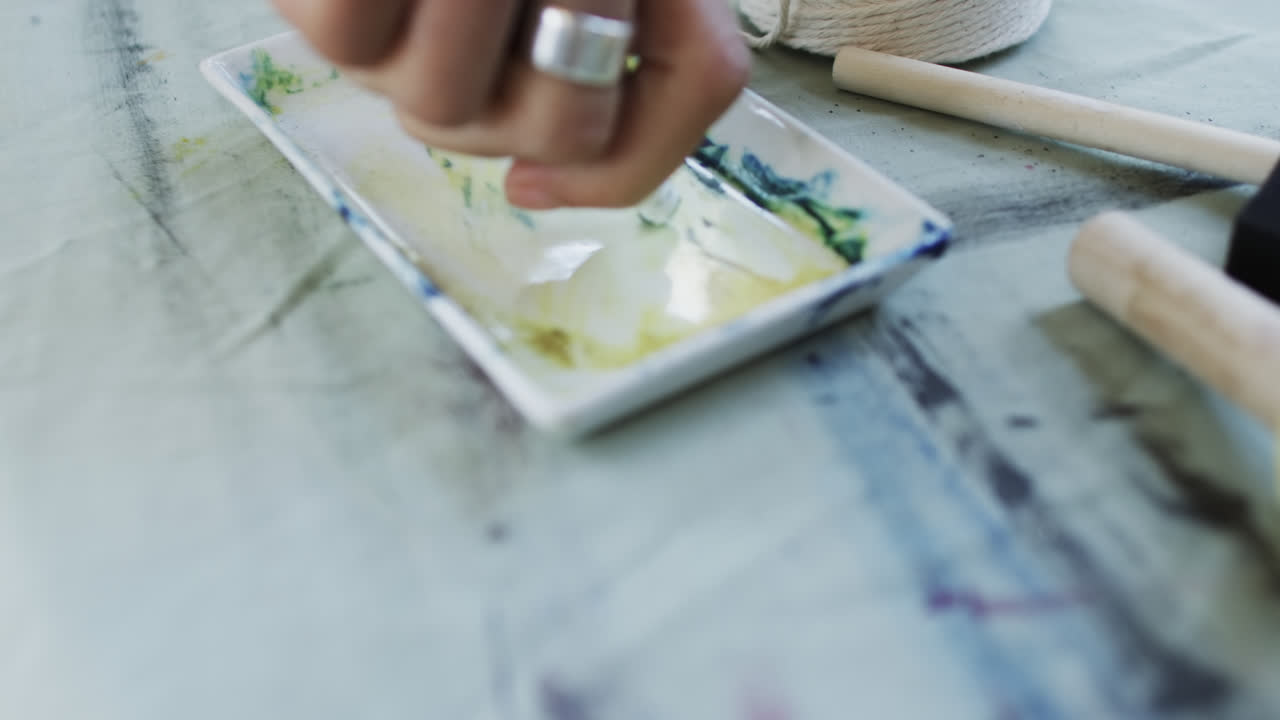 mano de una artista biracial preparando pintura en el estudio, cámara lenta