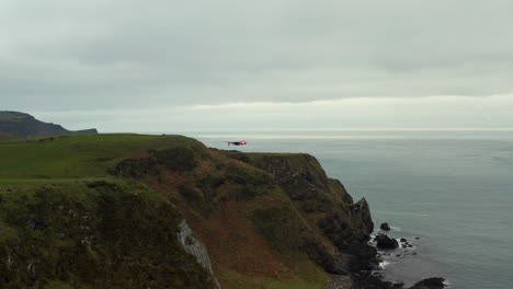 Drone-Con-Luces-Rojas-Vuela-Desde-Acantilados-Rocosos-Verdes-Hasta-El-Mar-En-La-Costa-Norte-De-Irlanda