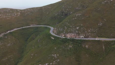 aerial shot of cars navigating a winding road through the outeniqua mountains, western cape, south africa. the drone captures the scenic route, showing the twisting path and surrounding mountain views