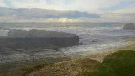 crashing waves against rocky coastline under cloudy sky with sun rays filtering