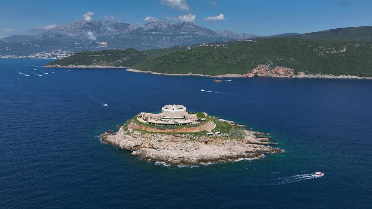 Small island with historic Mamula fort in blue sea, surrounded by boats and mountains