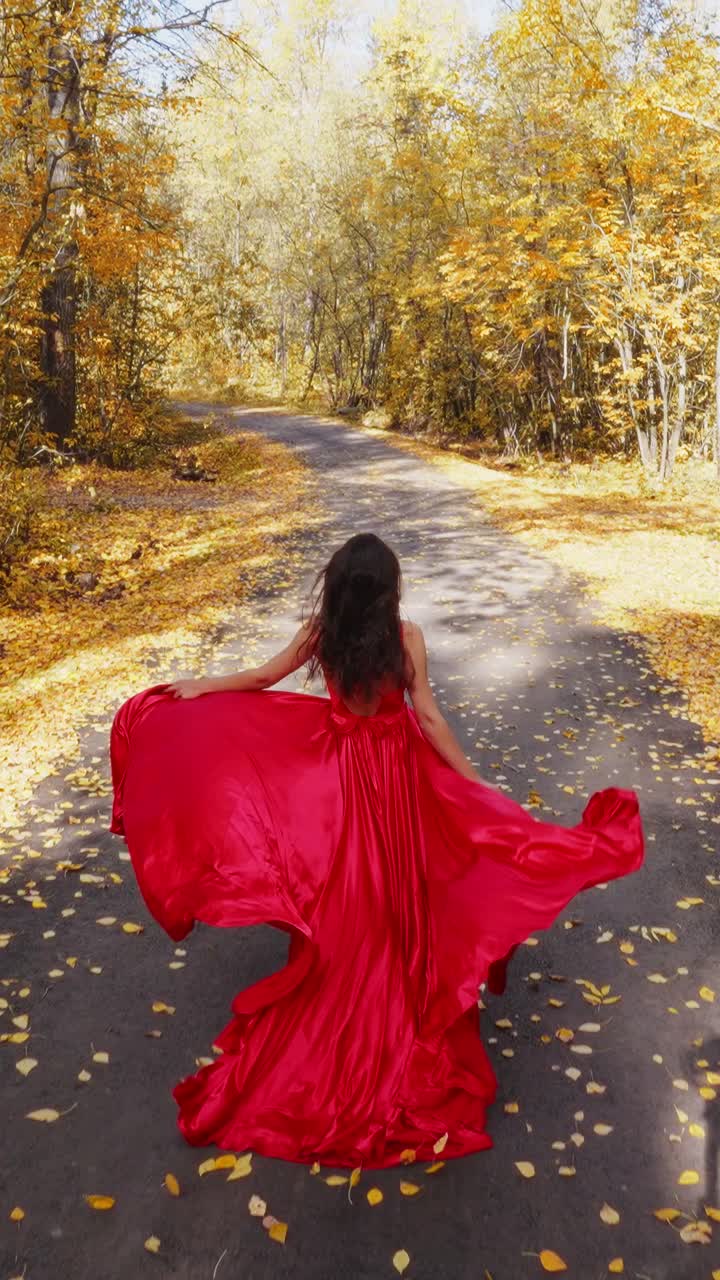 A Graceful Woman in a Flowing Red Dress Walks Through an Autumn Landscape Covered in Vibrant Fall Foliage, Capturing the Essence of Seasonal Beauty
