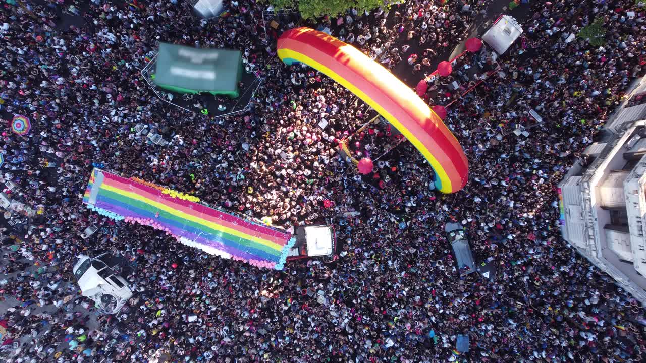 Overhead drone view of Buenos Aires LGBT gay pride parade in Plaza De Mayo square with colored truck and inflatable rainbow