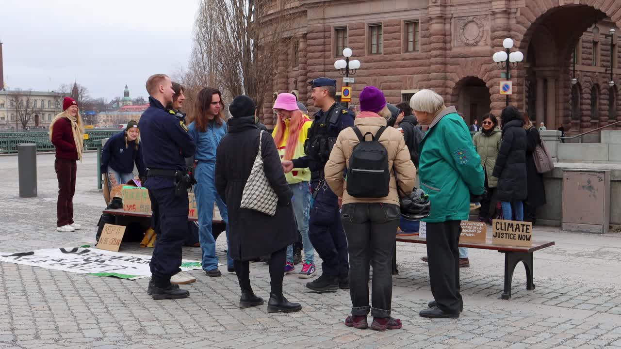 Protesters outside Swedish parliament with signs for climate justice talk to police officer